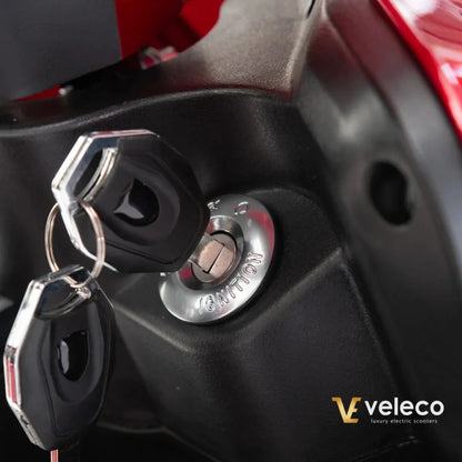 Na sliki je prikazan električni skuter znamke Veleco, model Draco. Vidna je ključavnica za vžig, ki je del sistema za zagon skuterja, skupaj z dvema ključi. Skuter ima sodoben dizajn in je zasnovan za udobno vožnjo.