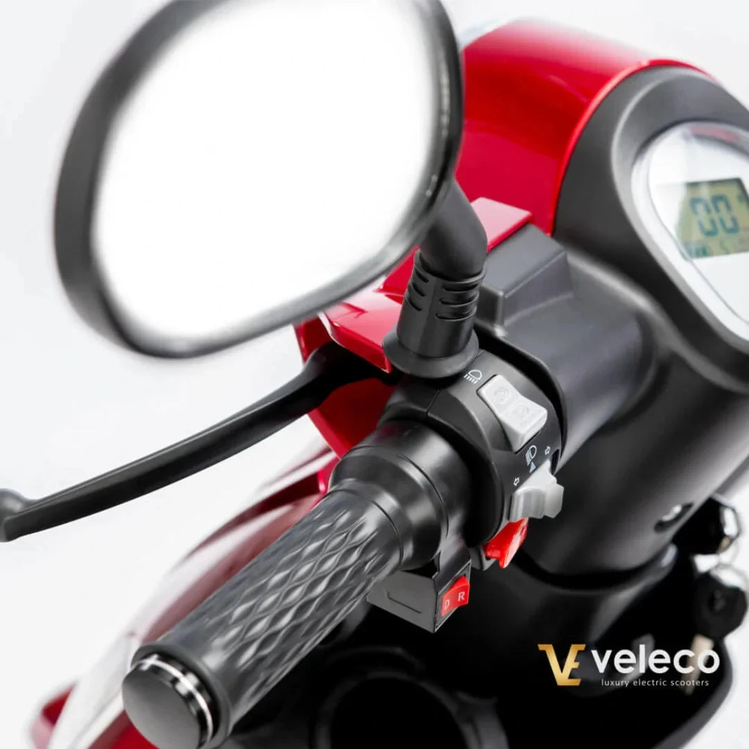 Izdelek na sliki je električni skuter znamke Veleco, model Draco. Na sliki je prikazan del krmila, kjer so vidni ročaj, stikala za upravljanje ter ogledalo. Barva skuterja je rdeča, kar mu daje športen videz. Na merilniku je prikazana hitrost, kar nakazuje na funkcionalnost in uporabnost skuterja.