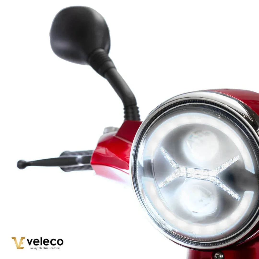 Izdelek je električni skuter, znamke Veleco, model Draco. Na sliki je prikazan del skuterja, ki vključuje krmilo, ogledalo in sprednjo luč. Skuter ima sodoben dizajn, z izrazito rdečo barvo in LED svetlobno tehnologijo.