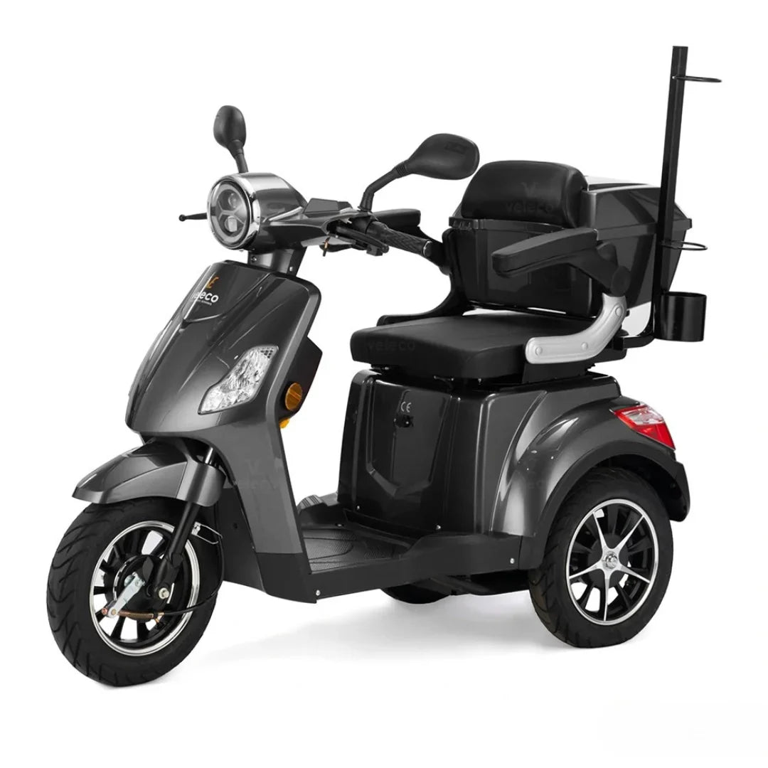 Izdelek je električni skuter, znamke Veleco, model Draco. Na sliki je prikazan skuter v temno sivi barvi, opremljen z udobnim sedežem in naslonom. Ima sprednje luči, krmilo z ročaji ter prostoren prostor za noge. Na skuterju je tudi nosilec za dodatno opremo, kar ga naredi praktičnega za vsakodnevno uporabo.