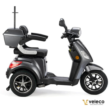 Izdelek na sliki je električni skuter, model Veleco Draco. Skuter ima tri kolesa, kar zagotavlja stabilnost, in je opremljen z udobnim sedežem ter prostorom za shranjevanje. Vidna sta tudi prednja luč in krmilo, kar nakazuje na funkcionalnost in uporabnost za mestno vožnjo. Zasnova je moderna in praktična, kar je značilno za znamko Veleco.