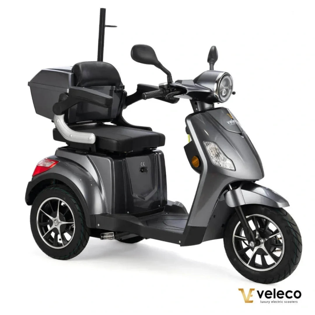 Izdelek na sliki je električni skuter, model Veleco Draco. Skuter ima tri kolesa, kar omogoča stabilno vožnjo, in je opremljen z udobnim sedežem ter prostorom za shranjevanje. Barva skuterja je siva, kar mu daje sodoben videz. Na sprednjem delu je vidna luč in krmilo, kar nakazuje na njegovo uporabnost v urbanem okolju.