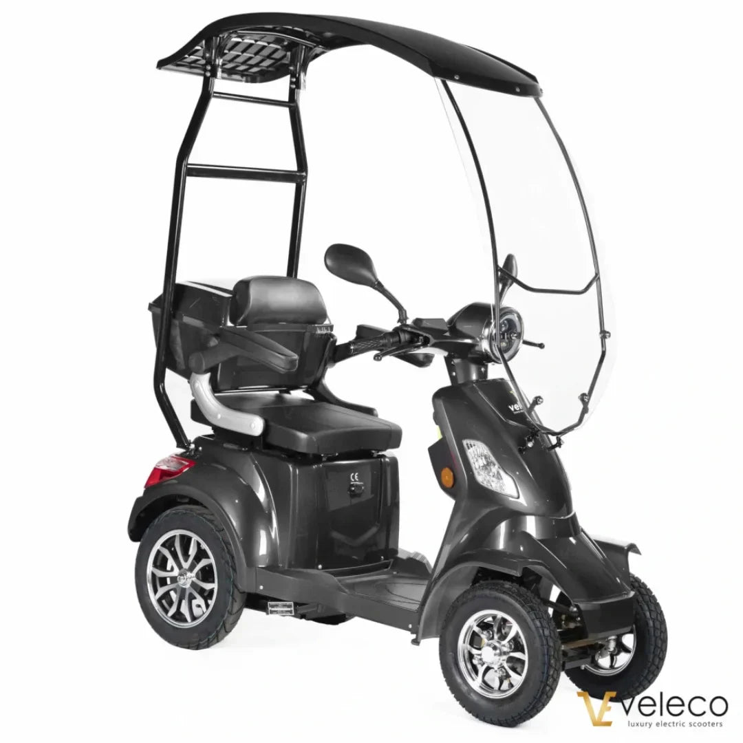 Izdelek je električni skuter, model Veleco Faster. Na sliki je prikazan skuter s tremi kolesi, kar omogoča stabilno vožnjo. Ima zaščitni pokrov, ki nudi zaščito pred vremenskimi vplivi, ter udobno sedežno površino. Zasnova je moderna in praktična, kar omogoča enostavno uporabo v urbanem okolju.