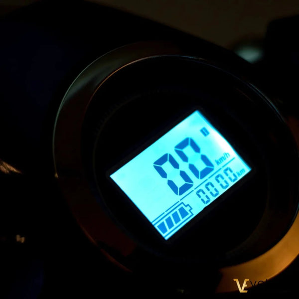 Izdelek je električni skiro znamke Veleco, model Faster. Na sliki je prikazan digitalni zaslon, ki prikazuje hitrost 0 km/h in prevoženo razdaljo 0,00 km. Zaslon vključuje tudi indikator napolnjenosti baterije, kar je pomembno za uporabnika.