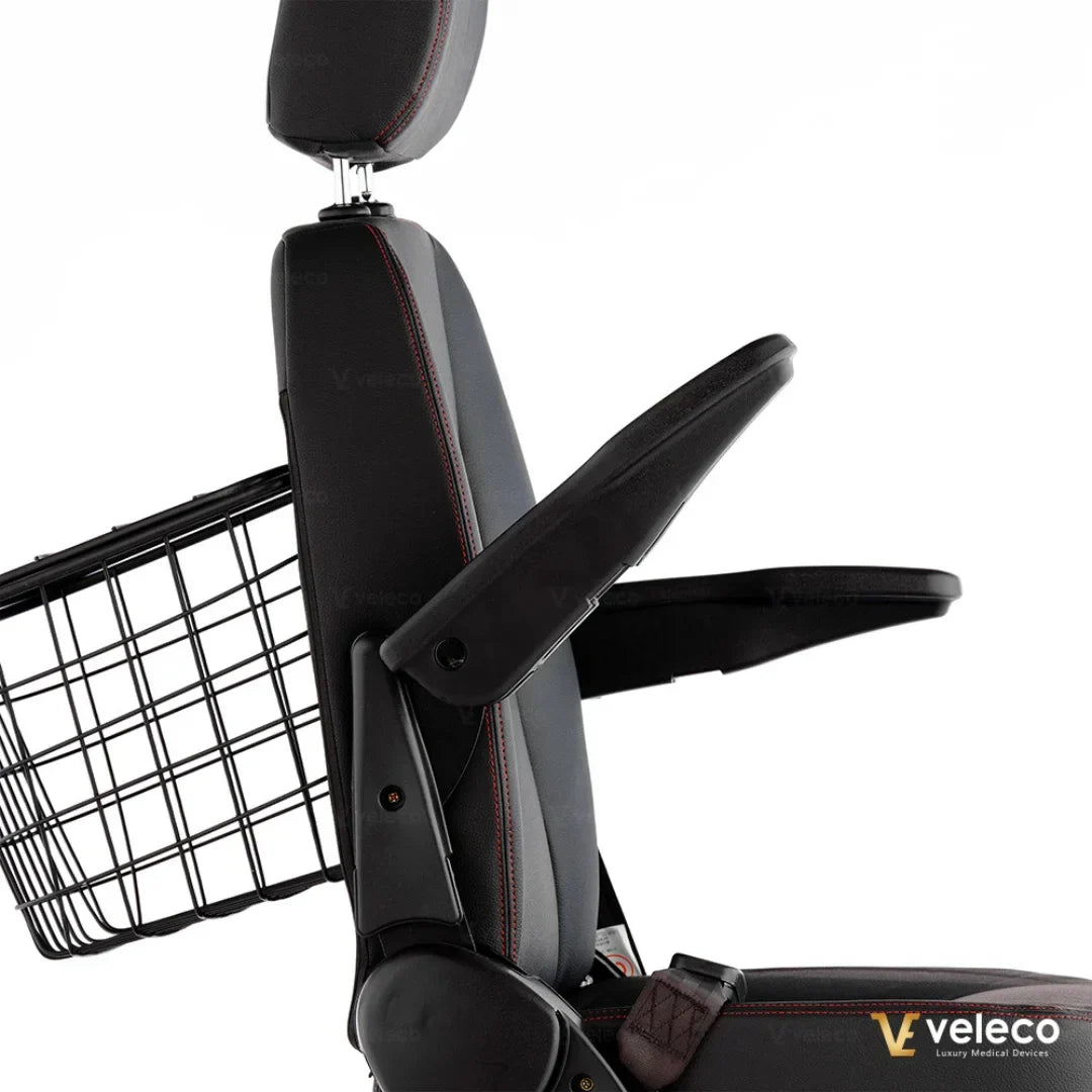 Izdelek na sliki je električni skuter, model Veleco Faster. Na sliki je prikazan sedež s podlogo in naslonjalom, ki imata nastavljive ročne naslone. Vidna je tudi košara na zadnjem delu skuterja, kar omogoča enostavno prenašanje osebnih predmetov. Sedež je oblazinjen in zasnovan za udobno vožnjo.