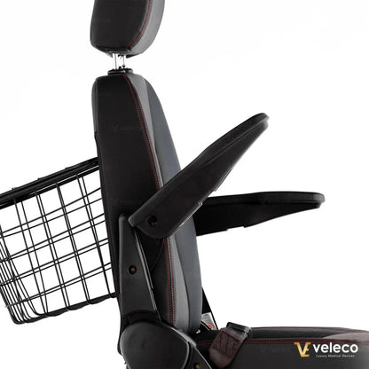 Izdelek na sliki je električni skuter, model Veleco Faster. Na sliki je prikazan sedež s podlogo in naslonjalom, ki imata nastavljive ročne naslone. Vidna je tudi košara na zadnjem delu skuterja, kar omogoča enostavno prenašanje osebnih predmetov. Sedež je oblazinjen in zasnovan za udobno vožnjo.