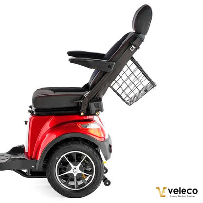 Izdelek je električni skuter, model Veleco Faster. Na sliki je prikazan stranski pogled skuterja, ki ima rdečo karoserijo, udobno sedežno površino ter naslonjalo. Vidna je tudi košara za shranjevanje, ki je pritrjena na zadnji del skuterja, kar omogoča praktično uporabo pri prevozu. Skuter je zasnovan za udobno in enostavno mobilnost.