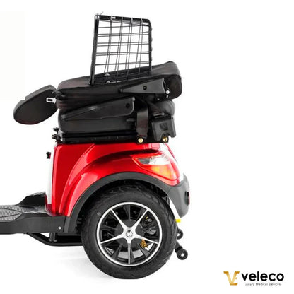 Izdelek na sliki je električni skuter, specifično model Veleco Faster. Na sliki je prikazana stranska perspektiva skuterja, ki je v rdeči barvi. Vidna sta tudi široka zadnja kolesa in prostoren sedež, ki je opremljen s hrbtnim naslonjalom. Na vrhu skuterja je nameščen koš za shranjevanje, kar povečuje njegovo funkcionalnost.