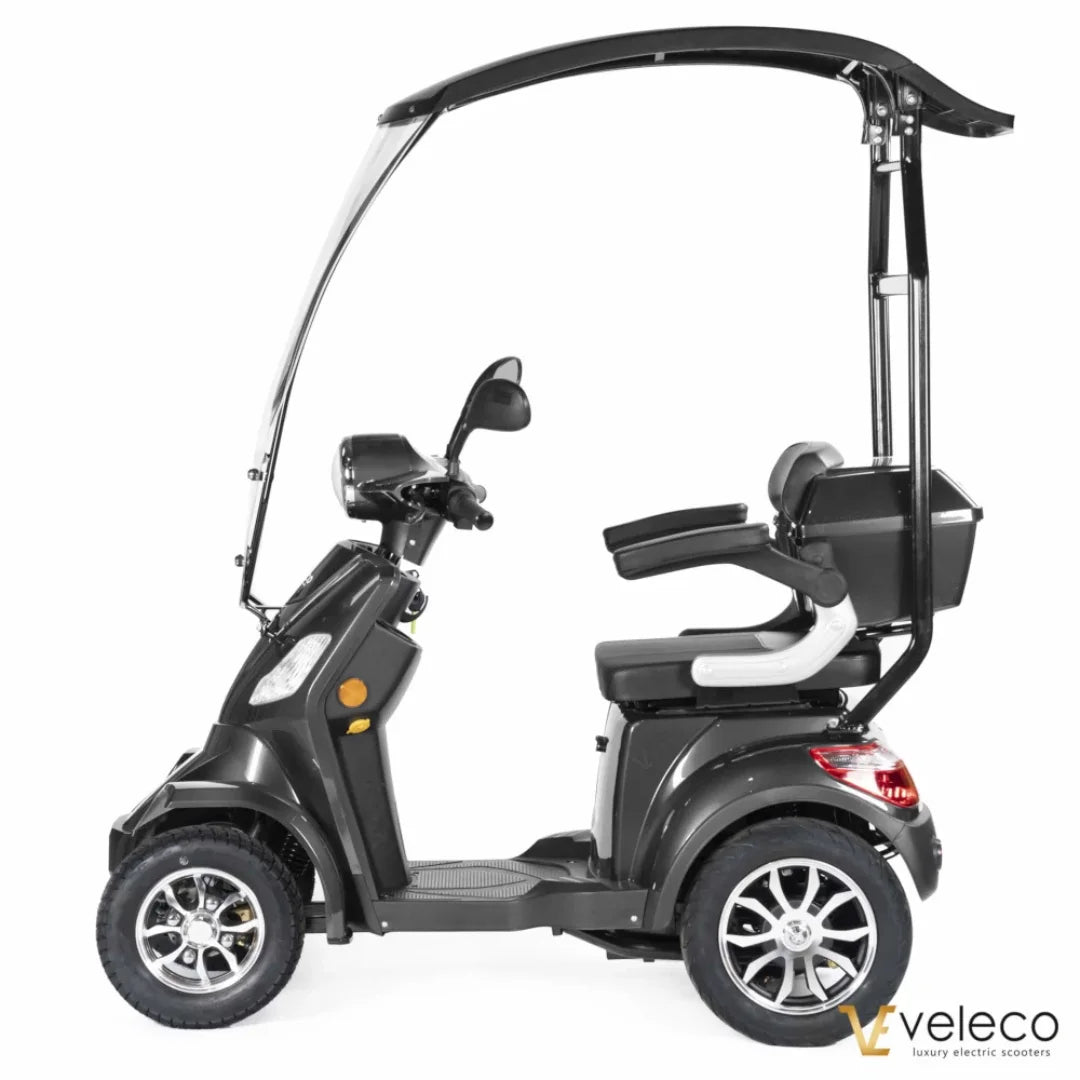 Izdelek na sliki je električni skuter, model Veleco Faster. Na sliki je prikazan stranski pogled skuterja, ki ima prostorno sedežno površino, zaščitni strešni del in udobno naslonjalo. Opremljen je s širokimi kolesi in ima moderno obliko, kar omogoča udobno vožnjo. Znamka Veleco je znana po luksuznih električnih skuterjih.