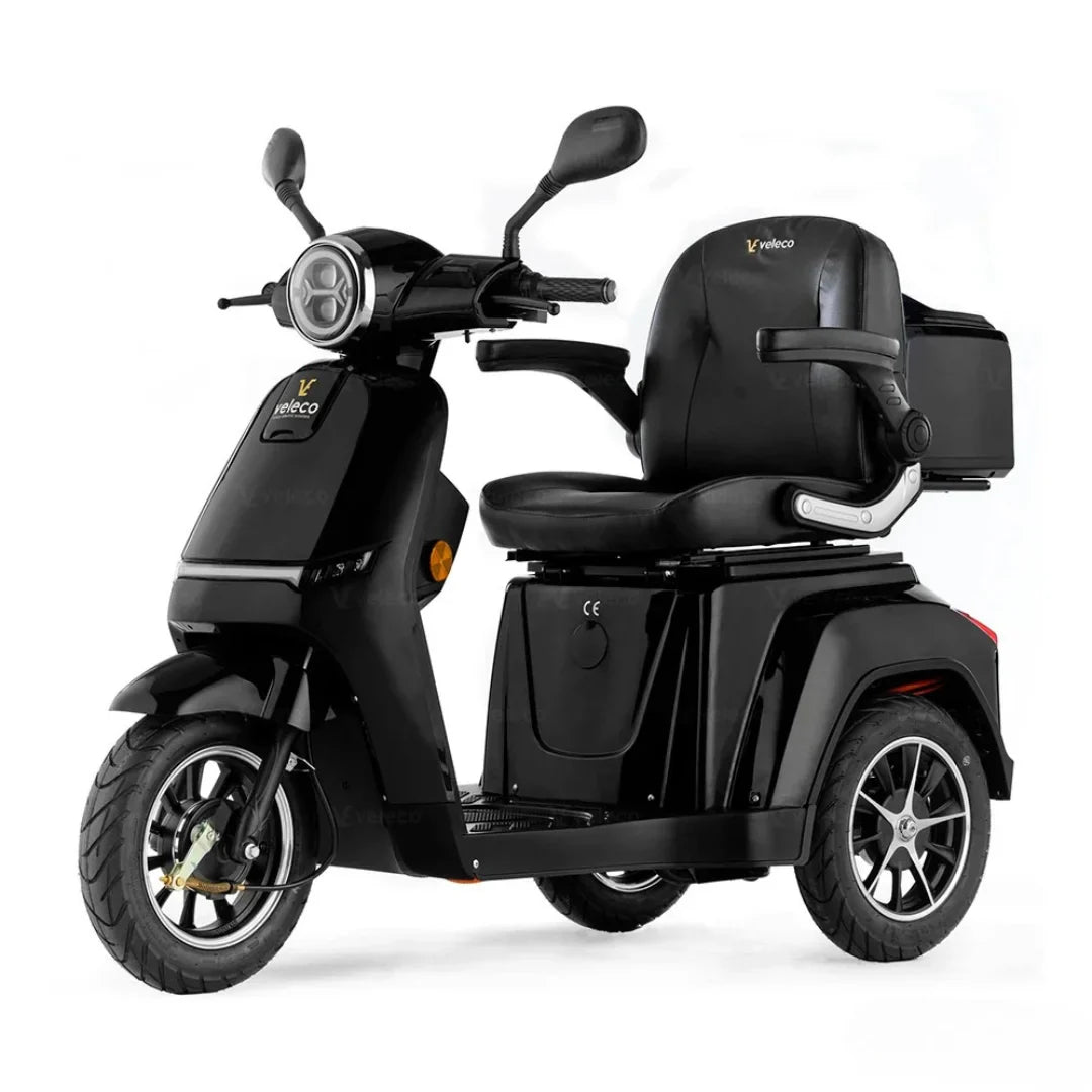 Izdelek je električni mobilni voziček, model Veleco Turris. Na sliki je prikazan voziček v črni barvi, opremljen z udobnim sedežem in krmilom. Ima tri kolesa, kar zagotavlja stabilnost, ter je zasnovan za enostavno upravljanje in udobno vožnjo. Na zadnjem delu vozička je vidna tudi majhna prtljažna enota.