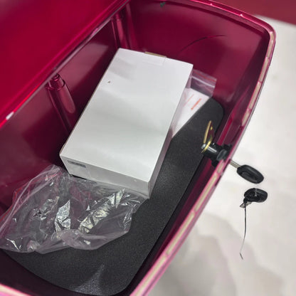 Izdelek je električni skuter s tremi kolesi, model Vigorous Vista 1. Na sliki je prikazan notranji prostor skuterja, kjer je vidna bela škatla, plastična vrečka in črna podlaga. Skuter ima tudi ključavnico, kar nakazuje na možnost zaklepanja. Barva notranjosti je rdeča, kar daje izdelku živahen videz.