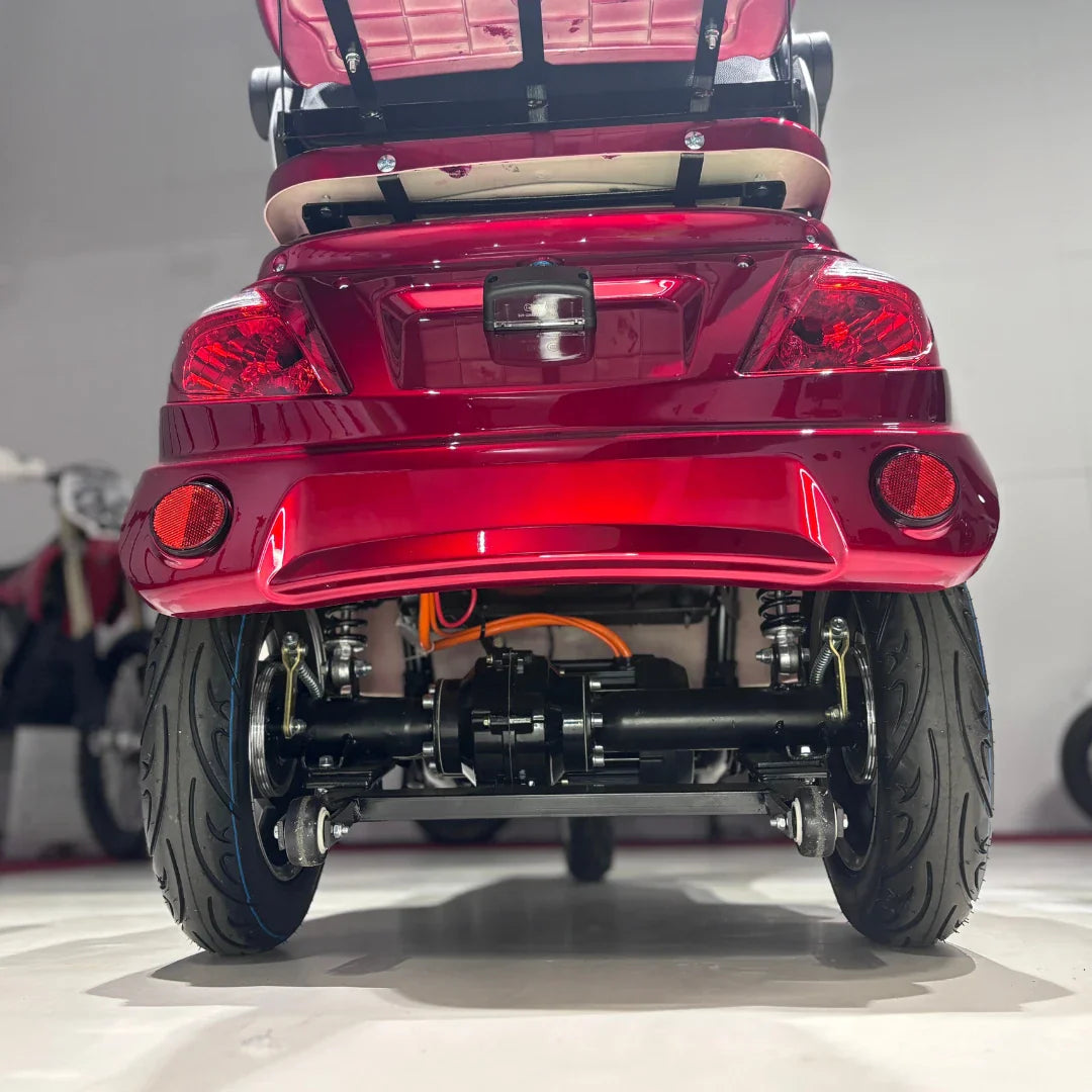 Izdelek je električni mobilni skuter s tremi kolesi, model Vigorous Vista 1. Na sliki je prikazan zadnji del skuterja v rdeči barvi, ki vključuje luči in del podvozja. Vidne so tudi pnevmatike in del motorja, kar nakazuje na robustno konstrukcijo in stabilnost vozila.