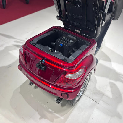 Izdelek je električni mobilni skuter s tremi kolesi, model Vigorous Vista 1. Na sliki je vidna zadnja stran skuterja, ki je v rdeči barvi. Odkrit je prostor za baterijo, ki je nameščena v zadnjem delu, ter priključki za polnjenje. Skuter ima tudi svetlobne elemente in vidne detajle, ki prispevajo k njegovemu modernemu videzu.