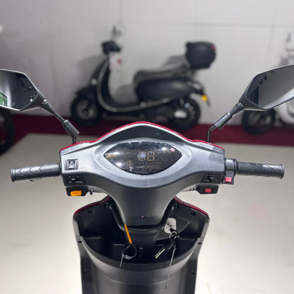 Izdelek na sliki je električni skuter z imenom Vigorous Vista 1. Na sliki je prikazan nadzorni panel, ki vključuje ročice za krmiljenje, zaslon za prikaz informacij ter ogledala. Skuter ima tri kolesa, kar omogoča stabilnejšo vožnjo, in je zasnovan za enostavno upravljanje. V ozadju so vidni tudi drugi skuterji.