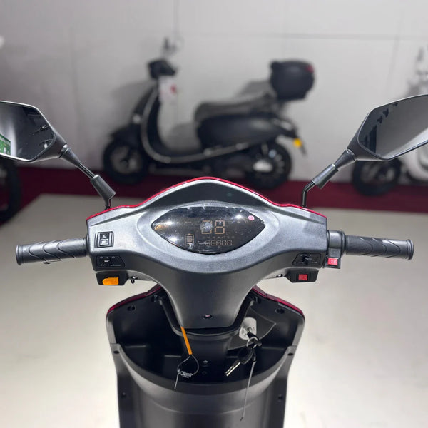 Izdelek na sliki je električni skuter z imenom Vigorous Vista 1. Na sliki je prikazan nadzorni panel, ki vključuje ročice za krmiljenje, zaslon za prikaz informacij ter ogledala. Skuter ima tri kolesa, kar omogoča stabilnejšo vožnjo, in je zasnovan za enostavno upravljanje. V ozadju so vidni tudi drugi skuterji.