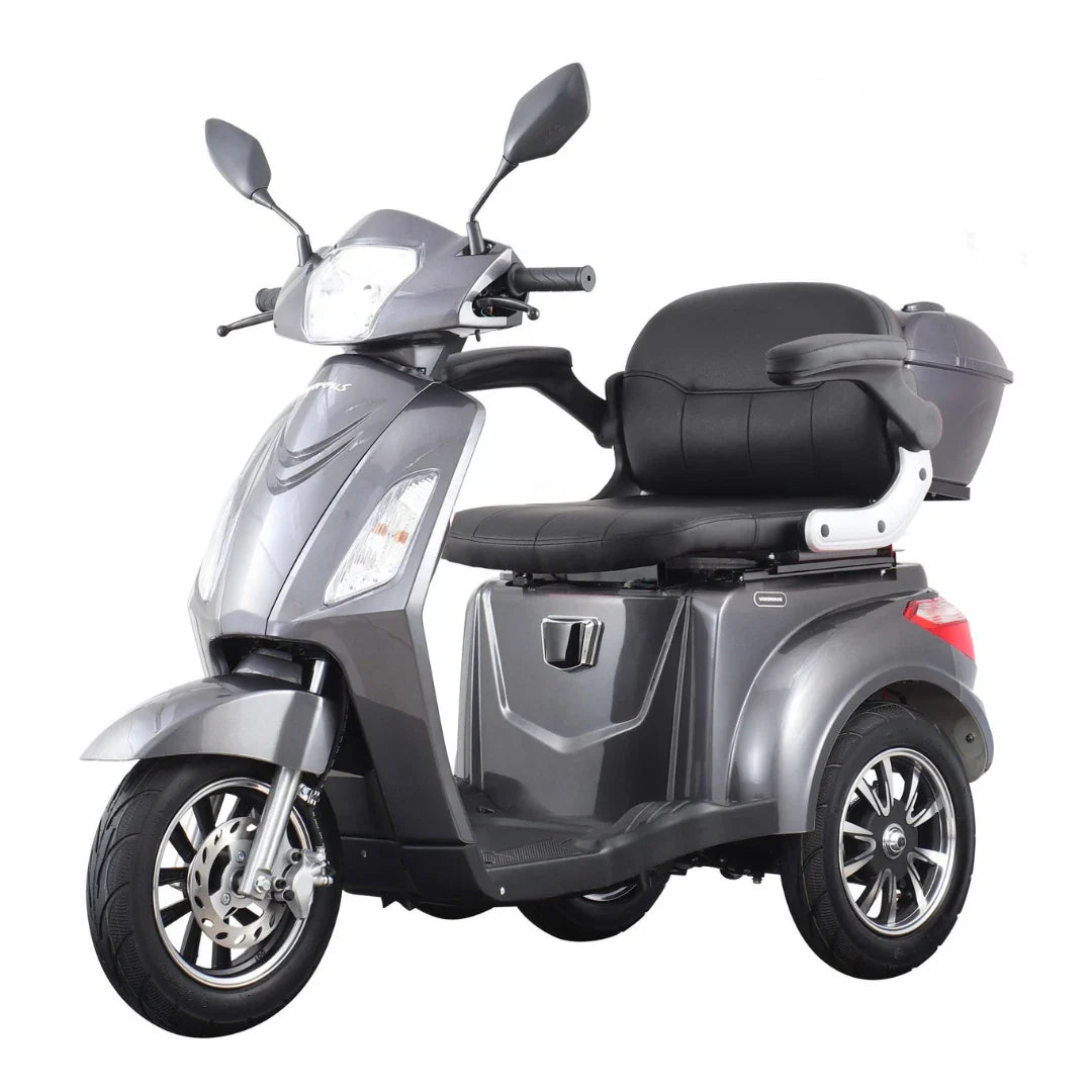 Izdelek je električni mobilni skuter s tremi kolesi, model Vigorous Vista 1. Na sliki je prikazan skuter v srebrni barvi, opremljen z udobnim sedežem in naslonjalom, ter dodatnim prostorom za shranjevanje. Ima tudi prednje luči in ogledala, kar nakazuje na njegovo uporabnost v urbanem okolju.