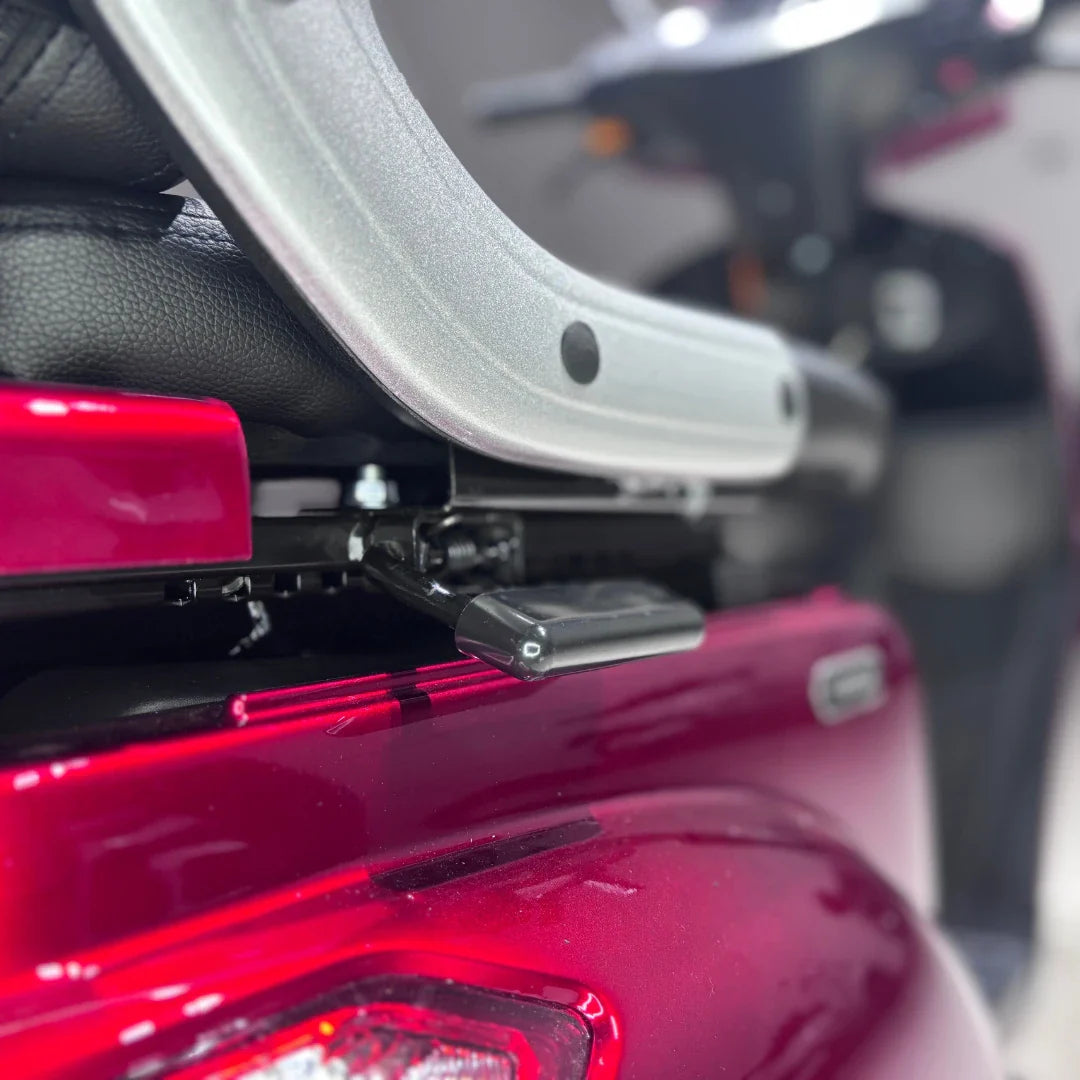 Izdelek je električni mobilni skuter s tremi kolesi, model Vigorous Vista 1. Na sliki je vidna podrobnost sedeža, ki je črn in udoben, ter del strukture skuterja v rdeči barvi. Oprema vključuje mehanizem za prilagajanje sedeža, kar omogoča enostavno dostopnost in udobje pri vožnji.