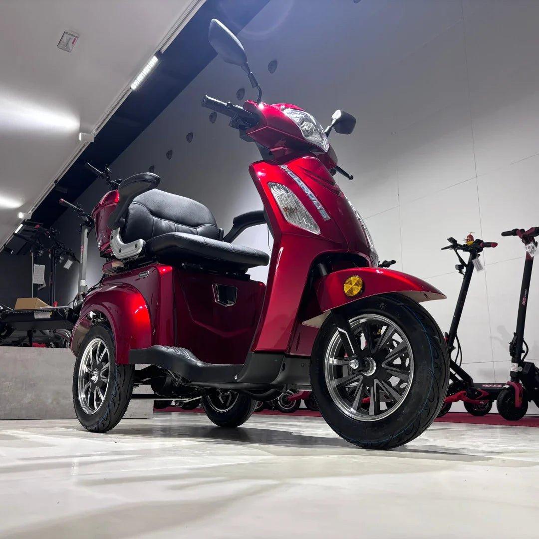 Izdelek na sliki je električni skuter s tremi kolesi, znamke Vigorous, model Vista 1. Skuter je v rdeči barvi in ima udobno sedežno površino ter prostoren prostor za shranjevanje. V ozadju so vidni tudi drugi električni skiroji, kar nakazuje, da gre za prodajno okolje.