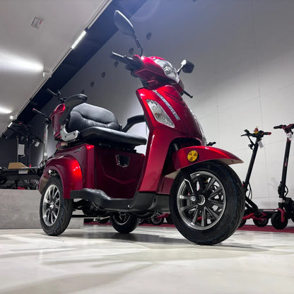 Izdelek na sliki je električni skuter s tremi kolesi, znamke Vigorous, model Vista 1. Skuter je v rdeči barvi in ima udobno sedežno površino ter prostoren prostor za shranjevanje. V ozadju so vidni tudi drugi električni skiroji, kar nakazuje, da gre za prodajno okolje.