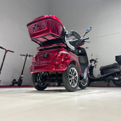 Izdelek na sliki je električni mobilni skuter s tremi kolesi, model Vigorous Vista 1. Skuter ima svetlo rdečo barvo in je zasnovan za udobno vožnjo. Vidna je tudi prtljažna enota na zadnjem delu, kar omogoča shranjevanje osebnih predmetov. V ozadju so vidni tudi drugi električni skuterji, kar nakazuje na okolje, kjer se ti izdelki prodajajo ali razstavljajo.