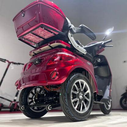 Izdelek na sliki je električni mobilni skuter z tremi kolesi, model Vigorous Vista 1. Značilna rdeča barva in oblikovanje nudita sodoben videz, medtem ko je na zadnjem delu skuterja vidna prtljažna enota, ki omogoča shranjevanje. Kolesa so široka, kar zagotavlja stabilnost, in skuter je opremljen s sodobnimi lučmi ter udobnim sedežem.