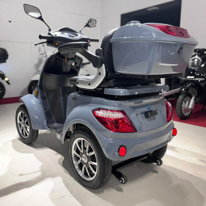 Izdelek je električni mobilni skuter s štirimi kolesi, model Vigorous Vista Q1. Na sliki je vidna zadnja stran skuterja, ki ima udoben sedež, prostoren prtljažnik in sodobno oblikovane luči. Skuter je v svetlo sivi barvi in ima elegantne aluminijaste platišča. Opremljen je z ogledali in upravljalnimi elementi na krmilu.