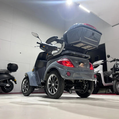 Izdelek na sliki je električni mobilni skuter, model Vigorous Vista Q1. Skuter ima štiri kolesa in se odlikuje po sodobnem dizajnu ter prostornem zadnjem predalu. Na sliki je jasno vidna njegova elegantna siva barva, športne platišča in ergonomična krmila, kar nakazuje na udobno vožnjo. V ozadju so vidni tudi drugi električni skuterji.