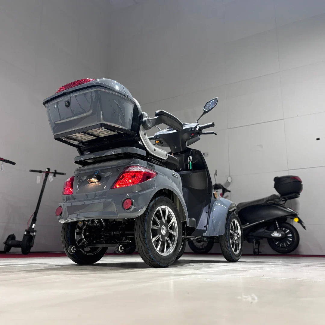 Izdelek na sliki je električni mobilni skuter, model Vigorous Vista Q1. Na sliki je vidna zadnja stran skuterja, ki ima štiri kolesa, prostoren prtljažnik na zadnjem delu ter udobno sedežno površino. Skuter je zasnovan za enostavno manevriranje in udobno vožnjo, kar ga naredi primernega za različne uporabnike. V ozadju so vidni tudi drugi električni skuterji.