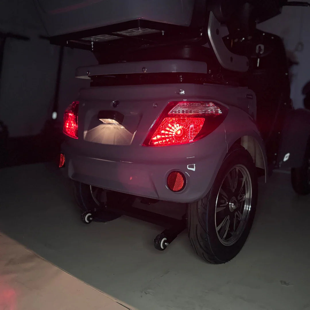 Izdelek je štirikolesni električni mobilni skuter, model Vigorous Vista Q1. Na sliki je vidna zadnja stran skuterja, ki ima rdeče luči in značilne oblike, kar kaže na njegovo zasnovo. Skuter je opremljen z večjimi kolesi in ima tudi svetlobne elemente, kar povečuje njegovo vidnost v temi.