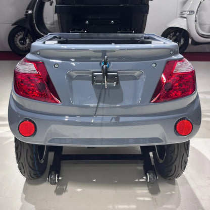 Izdelek je električni mobilni skuter, model Vigorous Vista Q1. Na sliki je prikazan zadnji del skuterja, kjer so vidne rdeče luči, ključavnica in široki pnevmatiki. Skuter ima tudi prostor za shranjevanje, ki je odprt, kar omogoča dostop do notranjosti. Barva skuterja je svetlo siva.