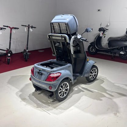 Izdelek je električni mobilni skuter, model Vigorous Vista Q1. Na sliki je prikazan skuter v svetlo sivi barvi, ki ima odprto zadnje pokrov, kar razkriva prostor za shranjevanje. V ozadju so vidni tudi drugi električni skuterji. Skuter ima štiri kolesa in je zasnovan za udobno vožnjo.