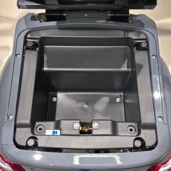 Izdelek je električni mobilni skuter, model Vigorous Vista Q1. Na sliki je prikazan odprt prostor za shranjevanje, ki se nahaja na zadnjem delu skuterja. V notranjosti je vidna plastična struktura brez dodatnih predmetov, kar nakazuje, da je prostor pripravljen za shranjevanje.