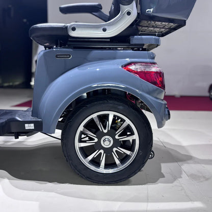 Izdelek je električni mobilni skuter, model Vigorous Vista Q1. Na sliki je prikazan del skuterja, ki vključuje zadnje kolo s športnim dizajnom platišča in del karoserije v svetlo sivi barvi. Vidna je tudi udobna sedežna garnitura ter del podvozja. Skuter je zasnovan za udobno in enostavno premikanje.