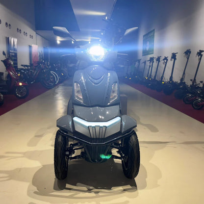 Izdelek na sliki je električni mobilni skuter, model Vigorous Vista Q1. Na sliki je prikazan sprednji del skutera, ki ima svetlo sondo in aerodinamično obliko. Skuter ima štiri kolesa, kar omogoča stabilno vožnjo, in je v svetlo sivi barvi. V ozadju so vidni tudi drugi električni skuterji, kar nakazuje, da gre za prodajno mesto ali razstavo.