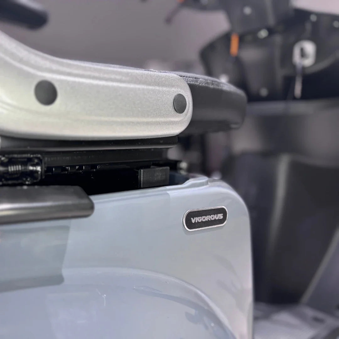 Izdelek je električni mobilni skuter, model Vigorous Vista Q1. Na sliki je del skuterja, kjer je vidna oznaka znamke "Vigorous" ter del sedeža in podvozja. Skuter je zasnovan za udobno vožnjo in mobilnost.