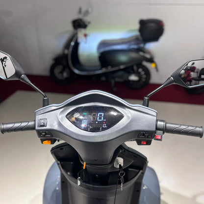 Izdelek na sliki je električni skuter, model Vigorous Vista Q1. Na sliki je vidna krmilna enota z digitalnim zaslonom, ki prikazuje hitrost in druge informacije. V ozadju je mogoče opaziti še druge skuterje, kar nakazuje, da gre za razstavo ali prodajno mesto.