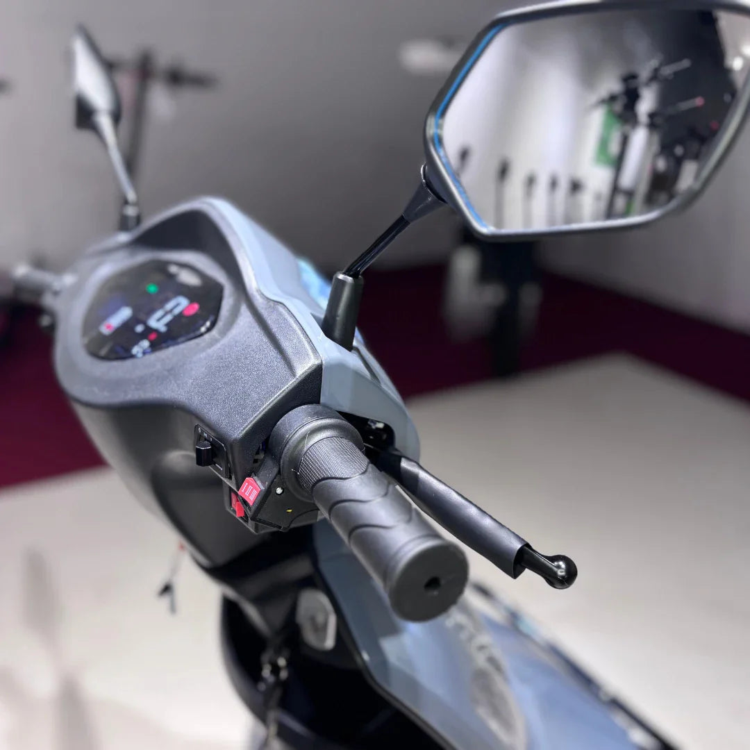 Izdelek na sliki je električni mobilni skuter, model Vigorous Vista Q1. Na sliki je prikazan del krmila, ki vključuje digitalni zaslon s prikazom informacij, ročico za plin ter ogledali. Skuter je zasnovan za udobno in enostavno vožnjo, kar je razvidno iz ergonomske oblike in opreme.