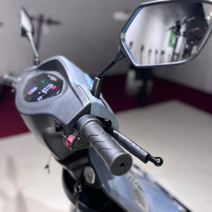 Izdelek na sliki je električni mobilni skuter, model Vigorous Vista Q1. Na sliki je prikazan del krmila, ki vključuje digitalni zaslon s prikazom informacij, ročico za plin ter ogledali. Skuter je zasnovan za udobno in enostavno vožnjo, kar je razvidno iz ergonomske oblike in opreme.