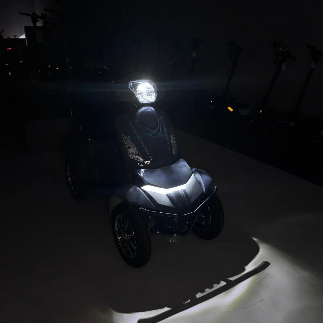 Izdelek na sliki je električni mobilni skuter z imenom Vigorous Vista Q1. Na sliki je vidna sprednja stran skuterja, ki ima svetlo na vrhu in elegantno obliko. Osvetlitev poudarja detajle na skuterju, medtem ko je ozadje temno, kar daje občutek modernosti in funkcionalnosti. Skuter je zasnovan za udobno in enostavno premikanje.