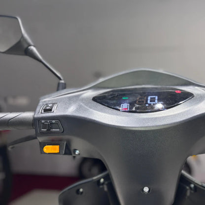 Izdelek je električni mobilni skuter, model Vigorous Vista Q1. Na sliki je prikazan del krmila, ki vključuje digitalni zaslon s prikazom hitrosti in stanja baterije, ter nekaj gumbov za upravljanje. Vidni so tudi ogledali, kar nakazuje na funkcionalnost in udobje pri vožnji.