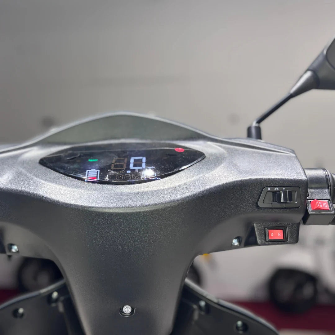 Izdelek je električni mobilni skuter, model Vigorous Vista Q1. Na sliki je prikazan nadzorni panel, ki vključuje digitalni zaslon za prikaz hitrosti in nivoja baterije, ter stikala za upravljanje. Vidni so tudi gumbi za izbiro smeri vožnje (naprej/ nazaj) in druge funkcije. Skuter je zasnovan za udobno in enostavno vožnjo.