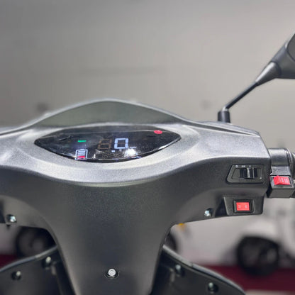 Izdelek je električni mobilni skuter, model Vigorous Vista Q1. Na sliki je prikazan nadzorni panel, ki vključuje digitalni zaslon za prikaz hitrosti in nivoja baterije, ter stikala za upravljanje. Vidni so tudi gumbi za izbiro smeri vožnje (naprej/ nazaj) in druge funkcije. Skuter je zasnovan za udobno in enostavno vožnjo.