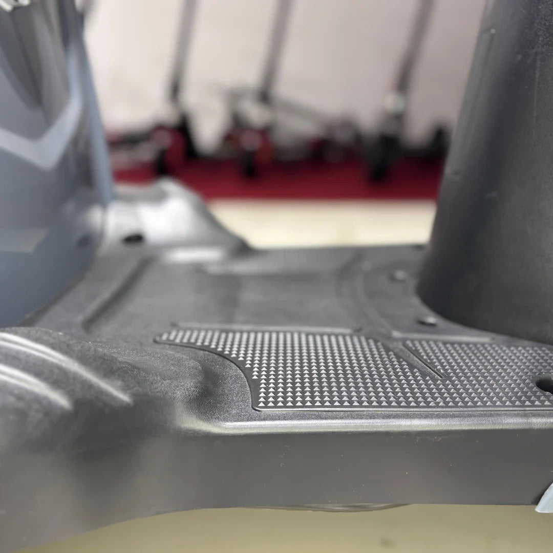 Izdelek je električni mobilni skuter, model Vigorous Vista Q1. Na sliki je prikazan del podlage skuterja, ki ima teksturirano površino za boljši oprijem. V ozadju so vidni drugi skuterji, kar nakazuje, da je izdelek del večje zbirke mobilnih naprav.