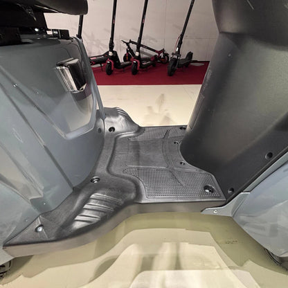 Izdelek je električni mobilni skuter, model Vigorous Vista Q1. Na sliki je prikazan del podnožja skuterja, ki ima teksturirano površino za boljši oprijem. V ozadju so vidni tudi drugi električni skiroji, kar nakazuje, da gre za okolje, kjer se ponujajo različni električni prevozi.