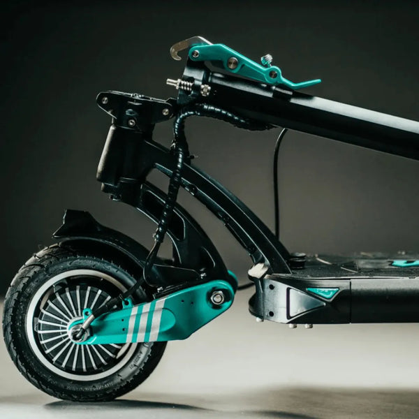 Na sliki je električni skiro znamke Vsett, model 9. Vidna je stranska perspektiva skiroja, ki prikazuje njegov zložljiv mehanizem, prednje kolo in del okvirja. Barvna kombinacija vključuje črno in svetlo modro, kar daje skiroju sodoben videz. Kolo ima robustno pnevmatiko in značilno obliko platišča.