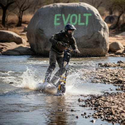 Na sliki je električni skiro znamke Vsett, model 11 Super. Na skiroju vozi oseba, ki se premika po vodi, kar povzroča škropljenje vode okoli njega. V ozadju je vidna velika skala z napisom "EVOLT". Oseba je oblečena v zaščitno opremo, kar nakazuje, da se nahaja v naravnem okolju, verjetno na avanturistični vožnji.