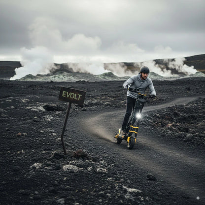 Izdelek je električni skiro znamke Vsett, model 11 Super. Na sliki je vidna oseba, ki vozi skiro po slikovitem terenu, obdanem z vulkanskimi kamni in dimniki. Oznaka "EVOLT" na znak ob poti dodaja zanimiv kontekst okolju. Oseba nosi čelado in udobna oblačila, kar nakazuje na aktivno uporabo skiroja v naravi.