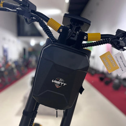 Na sliki je prikazan električni skiro znamke Vsett, model 11 Super. Na krmilu je vidna črna torbica z logotipom Vsett, ki služi za shranjevanje manjših predmetov. Ročaji so opremljeni z rumenimi dodatki, kar daje skiroju športen videz. V ozadju so vidni drugi električni skiroji, kar nakazuje, da gre za prodajno okolje.