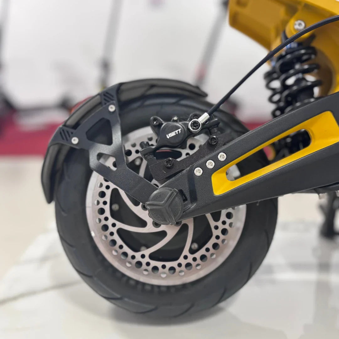 Izdelek na sliki je električni skiro, model VSETT 11 Super. Vidna je zadnja kolesna enota, ki vključuje disk zavore in vzmetenje. Kolo ima široko pnevmatiko, kar omogoča boljšo stabilnost in udobje pri vožnji. Na skiroju je tudi oznaka znamke VSETT.