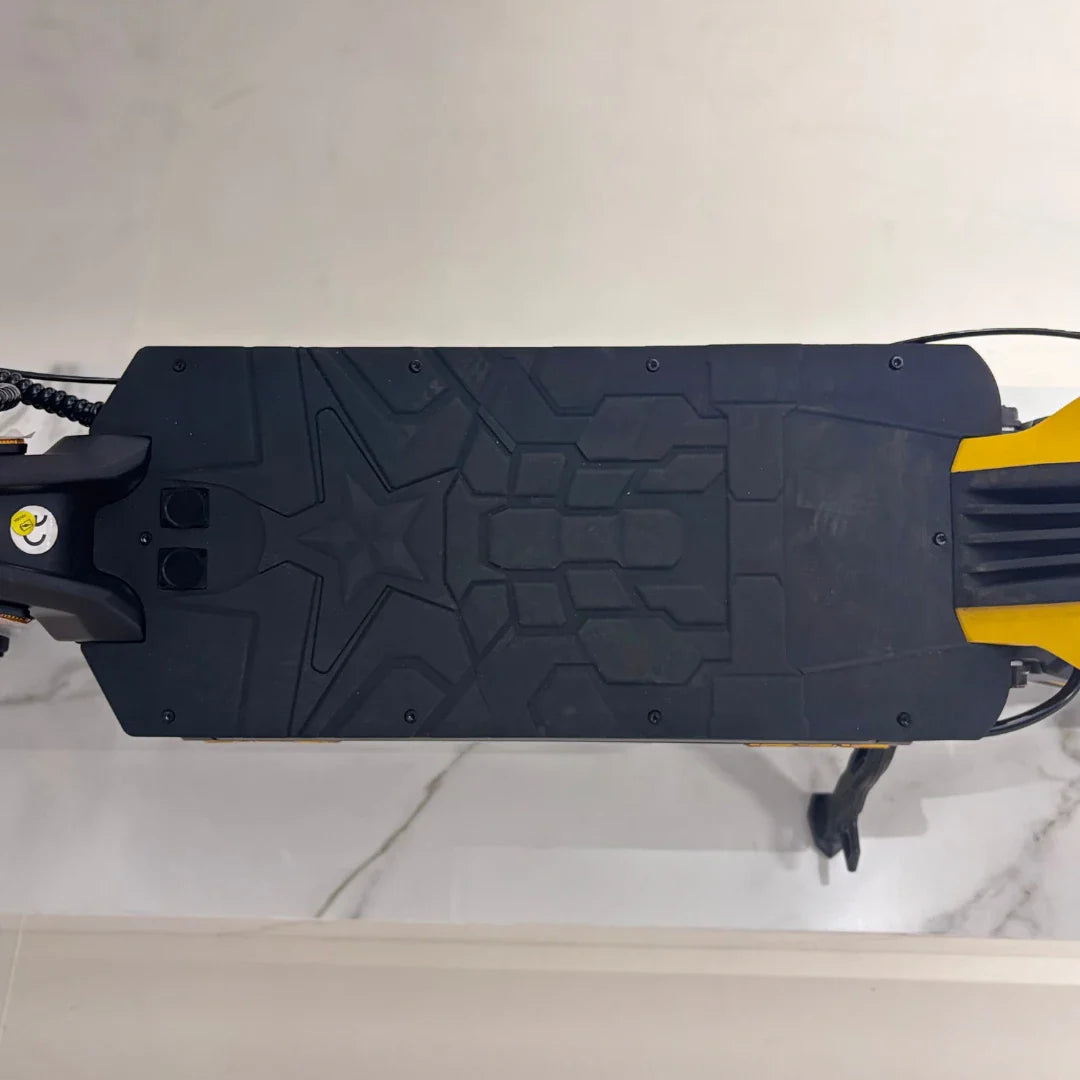 Izdelek na sliki je električni skiro, model Vsett 11 Super. Na sliki je vidna platforma skiroja, ki ima teksturirano površino za boljši oprijem, ter del okvirja v rumeni barvi. Viden je tudi del krmila in kabli, kar nakazuje na funkcionalnost in zasnovo skiroja.